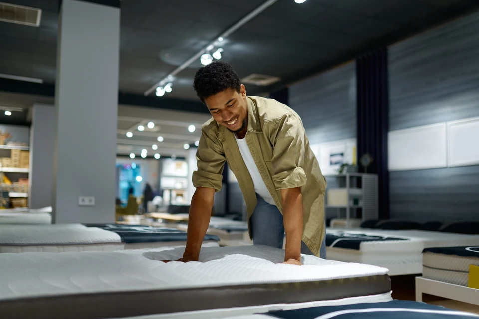 Une femme examine un matelas dans un magasin de mobilier, testant la fermeté en appuyant sa main sur la surface