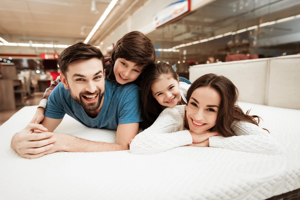 Femme souriante allongée sur un matelas blanc dans un magasin de literie, testant le confort d'un lit